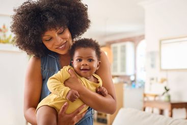 Loving Mother Indoors At Home Standing Cuddling Baby...