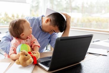 father with baby working on laptop at home office