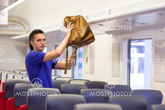 Young man putting luggage into overhead locker at train