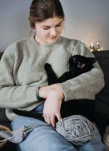 Woman cuddling black cat on sofa, surrounded by yarn....