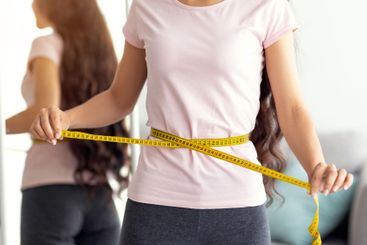 Unrecognizable Indian lady measuring her waist with tape...