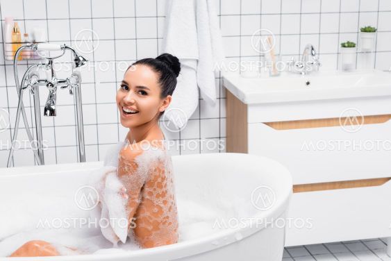 Brunette woman in foam smiling at camera while taking...