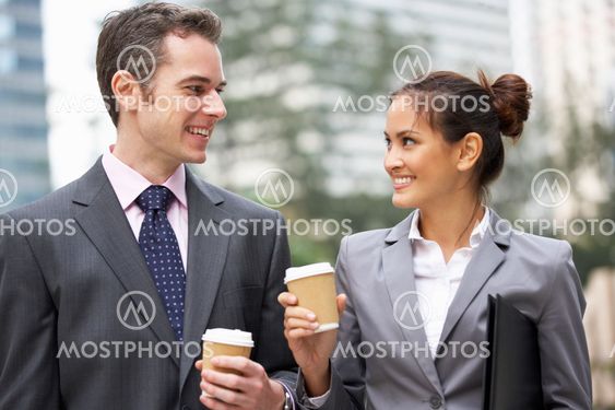 Businessman And Businesswoman Chatting In Street Holding Takeaway Coffee