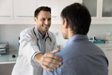 Cheerful male doctor touching shoulder of patient