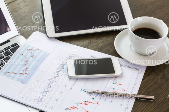 Laptop, tablet , smartphone and coffee cup with financial documents on wooden table
