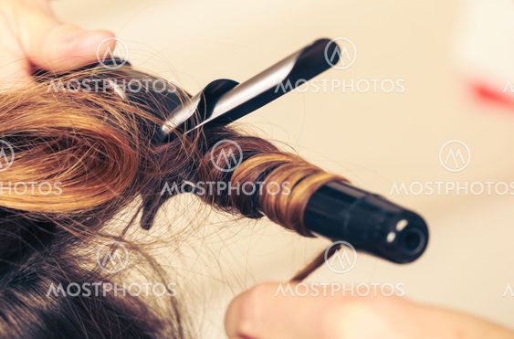 Stylist curling hair for young woman.