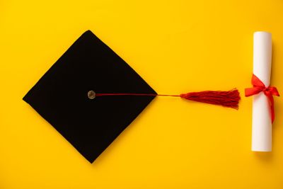 Top view of diploma and graduation cap with red tassel...