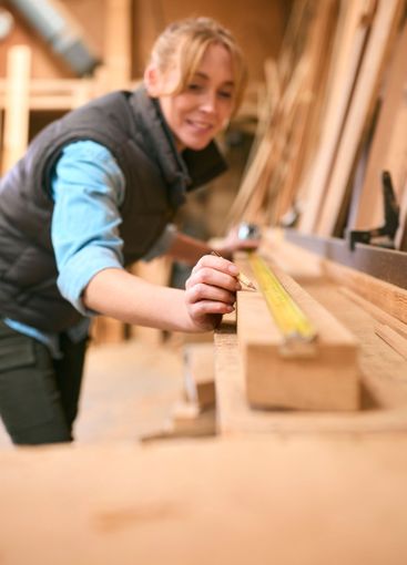 Female Carpenter Working In Woodwork Workshop Measuring...