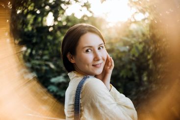 Smiling woman looking back with sunlight and forest...