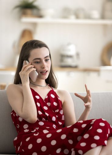 Focused gen z woman sitting on sofa speaking on phone