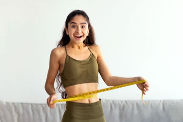 Full length portrait of slim Indian woman measuring her...