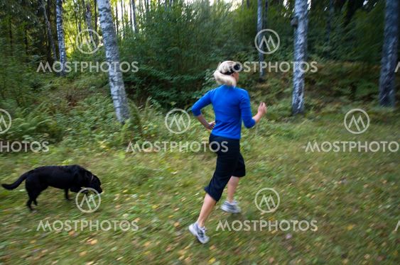Kvinna springer med hunden i skogen