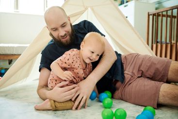 Baby, father and play with balls in home by tent, having...