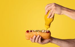 Young man applying mustard on fresh juicy hotdog, orange...