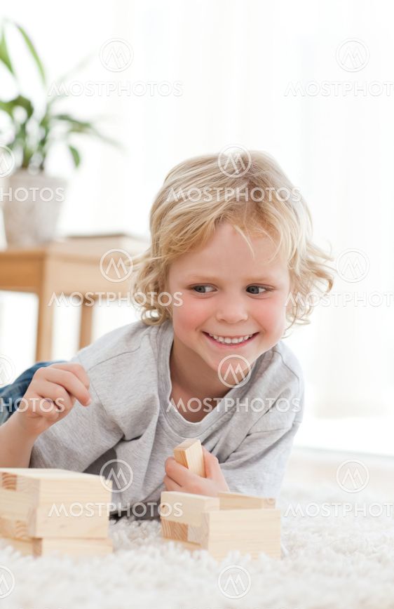 Cute little boy playing with dominoes lying on the floor