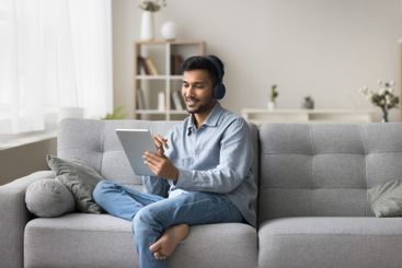 Smiling young male in headset sit on sofa use tablet