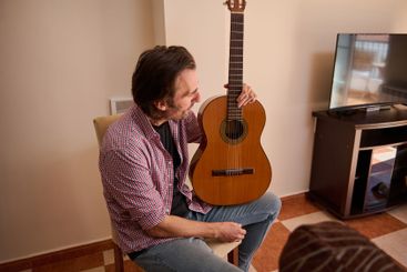 Man Holding a Classical Guitar While Sitting Indoors