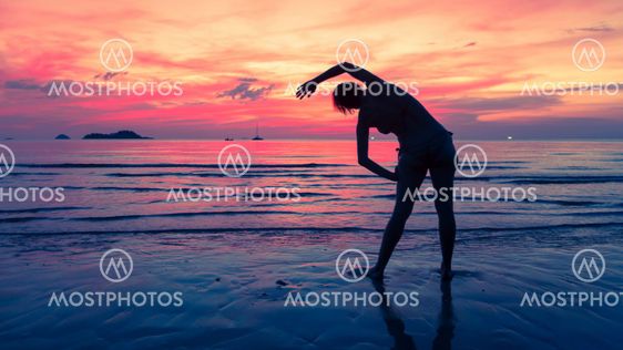Female silhouette performs physical exercises on the beach after sunset.