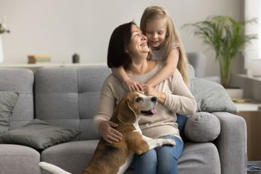 Lovely kid cuddles older grandma sit on sofa with dog