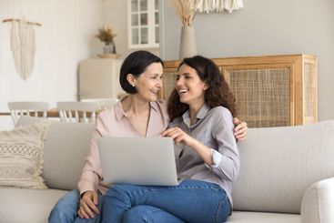 Joyful young daughter mature mother sitting on couch...