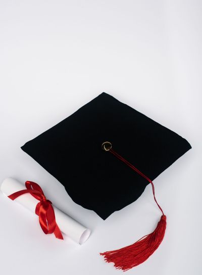 Black graduation cap with red tassel and diploma on...