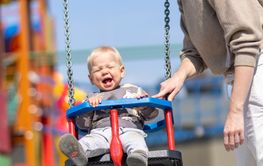 Mother pushing her infant baby boy child on a swing on...