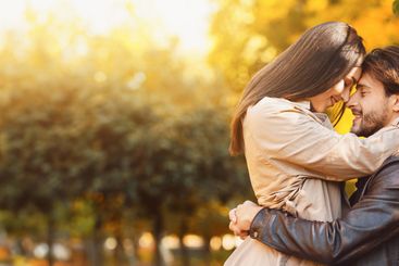 Loving couple cuddling over golden forest background