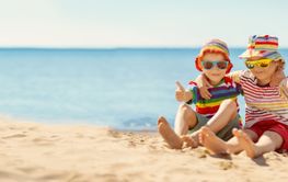 Happy children sitting on the sand beach in sunny day.