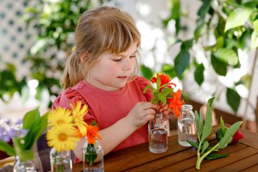 Little preschool girl making flower bouquet at home....
