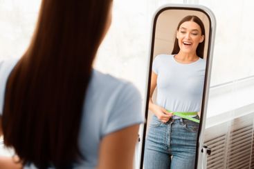 Excited Girl Measuring Thin Waist With Tape Standing...