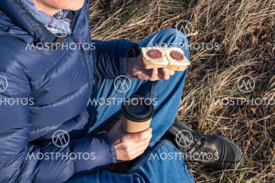 A man sits on the grass in the fall and eats a cheese...