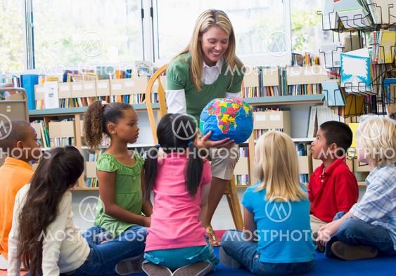 Kindergarten teacher and children looking at globe in...