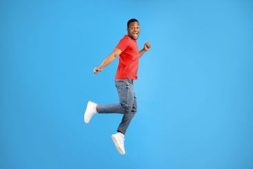 Carefree african american man jumping smiling to camera,...