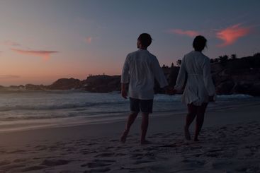 Couple, holding hands and walking by sunset on beach,...