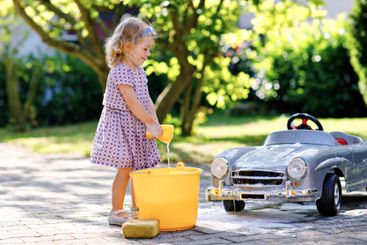 Cute gorgeous toddler girl washing big old toy car in...
