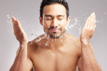 Man, water splash and cleaning face in studio for...