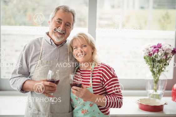Smiling senior couple holding glass of wine in kitchen