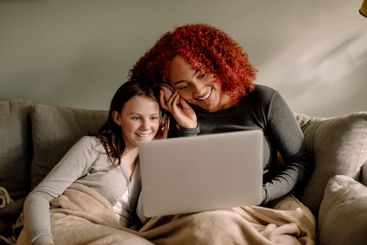 Smiling young woman and teenage girl watching movie...