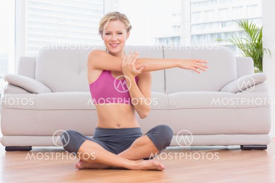 Smiling blonde sitting in lotus pose stretching arms
