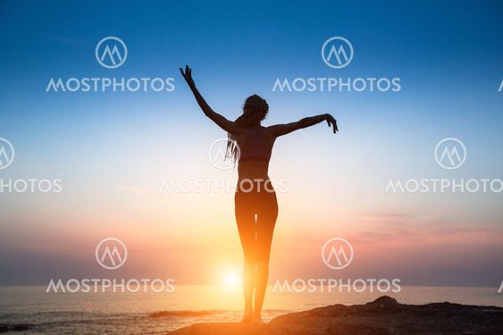Silhouette flexible girl moves in a dance on the shore of the sea during twilight.