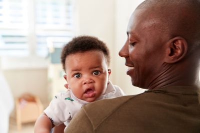 Proud Father Cuddling Baby Son In Nursery At Home