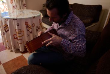 Man tuning a classical guitar indoors in a relaxed home...