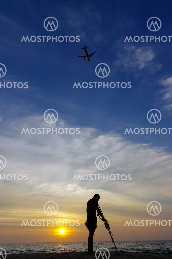 Treasure hunter with Metal detector on the sunset the beach