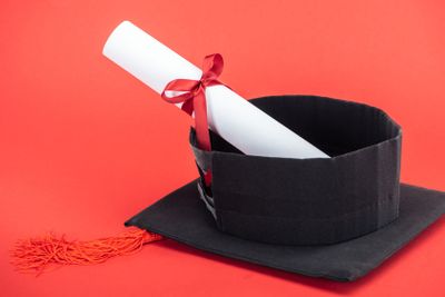 Academic cap with tassel and diploma with ribbon on red...