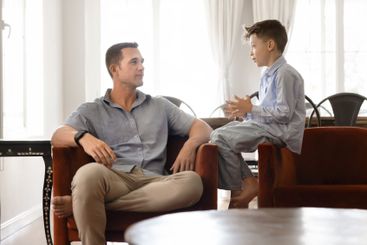 Positive handsome dad talking to son kid at home