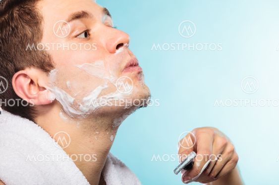 Young man shaving using razor with cream foam.