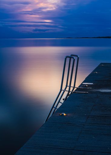 Reflections on calm water at dusk by a wooden dock with...