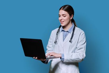 Portrait of smiling female doctor using laptop on blue...