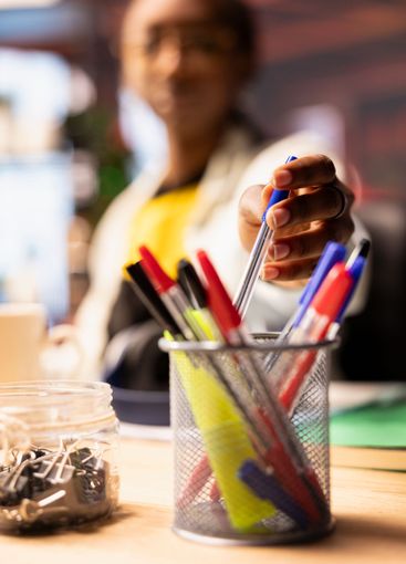 Woman in home office reaching for pencil from desk...