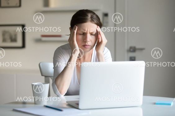 Portrait of woman at the desk holding tight her temples
